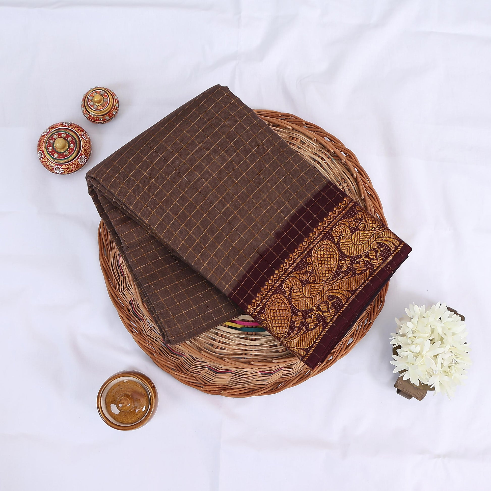 Sungudi cotton saree with gold zari checks body and maroon peacock motif border folded top view on wicker basket