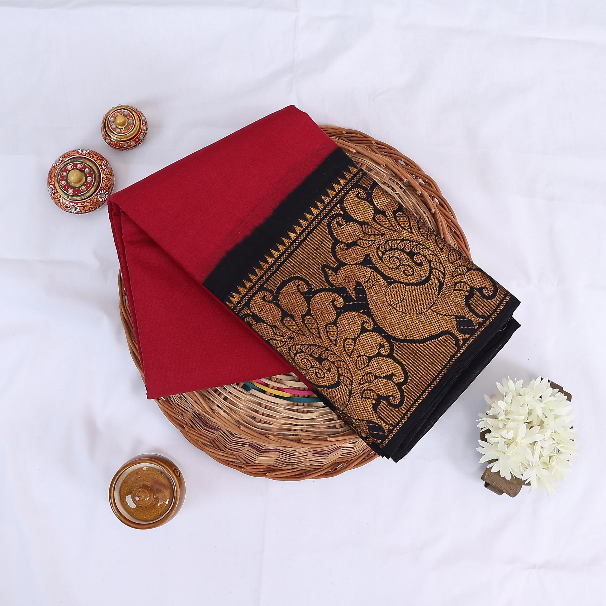 Sungudi cotton saree with gold zari floral border in red and black folded on wicker basket top view