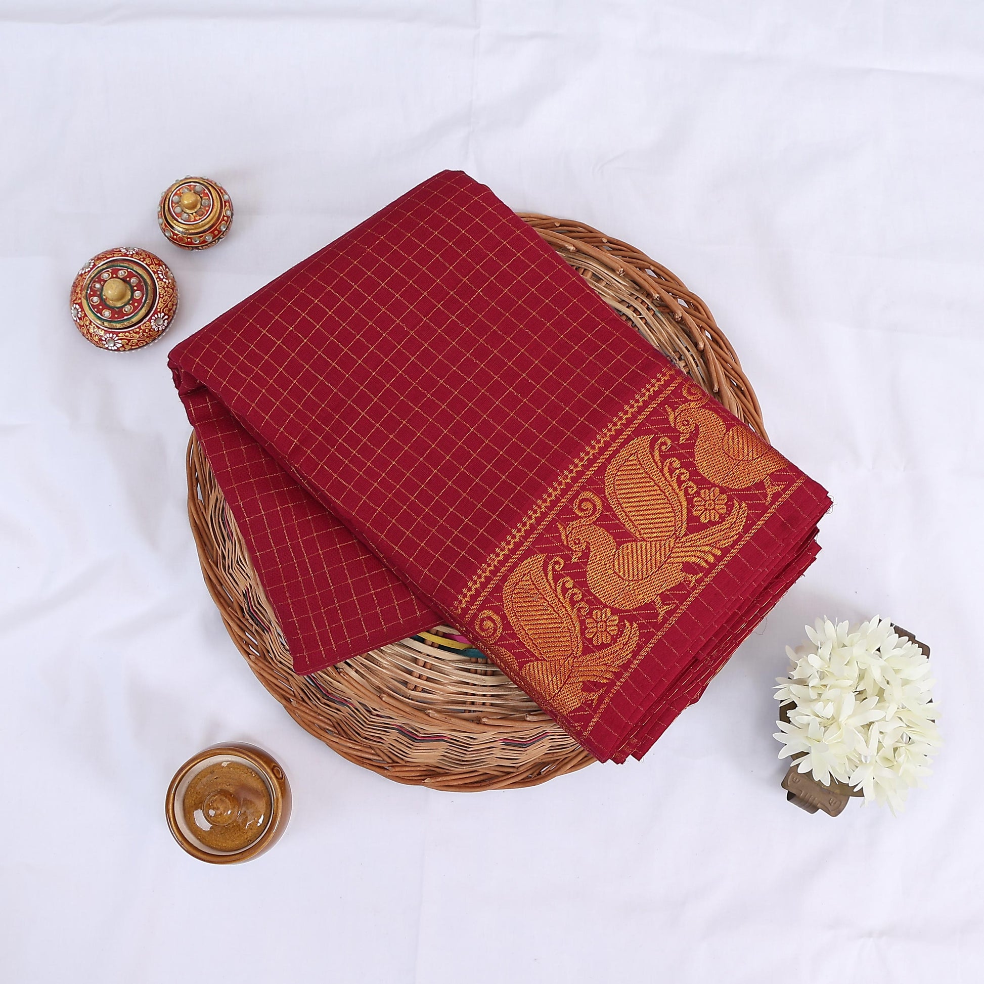 Sungudi cotton saree with gold zari checks body and red peacock motif border folded top view on wicker basket