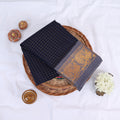 Sungudi cotton saree with gold zari checks body and grey peacock motif border folded top view on wicker basket