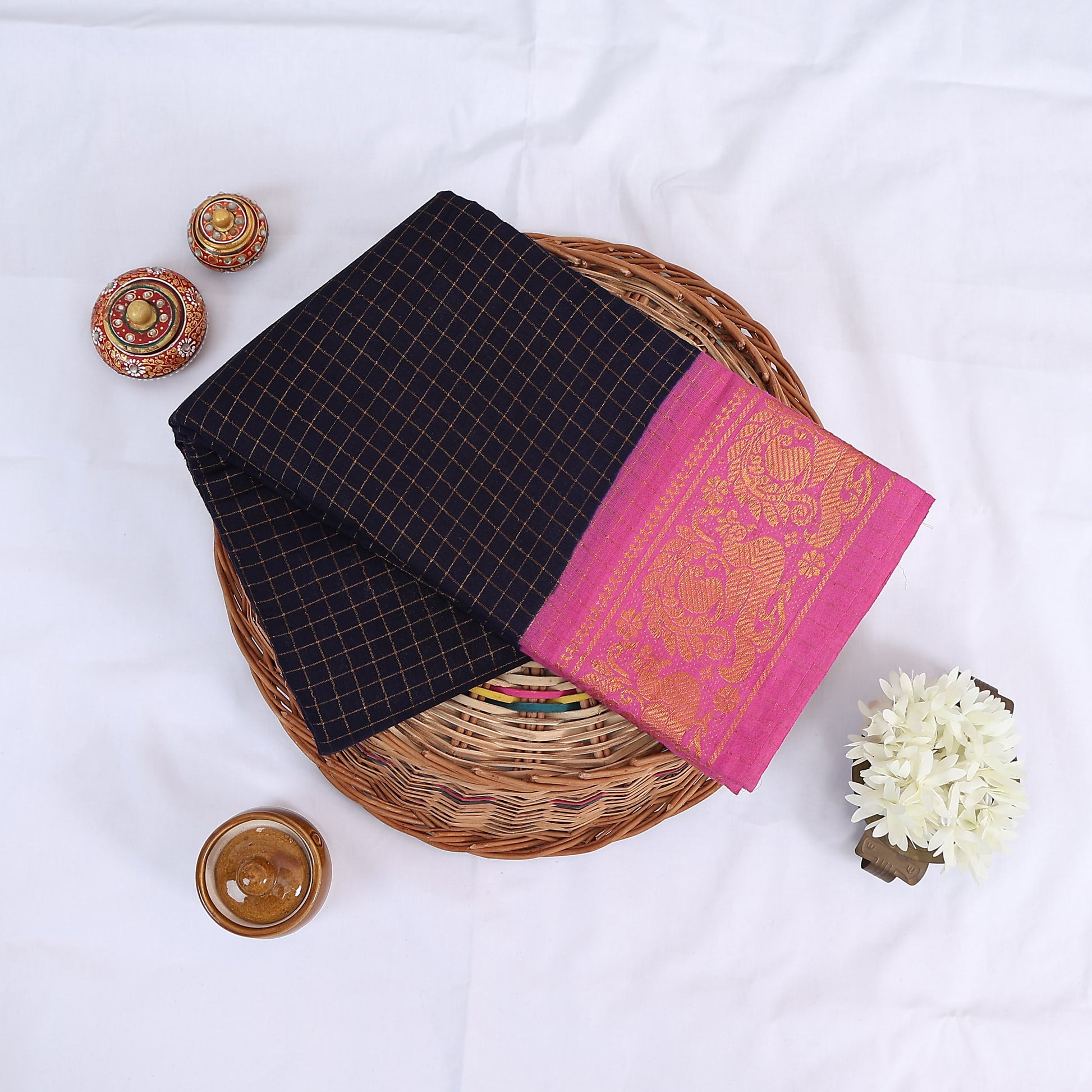 Sungudi cotton saree with gold zari checks body and royal blue peacock motif border folded top view on wicker basket