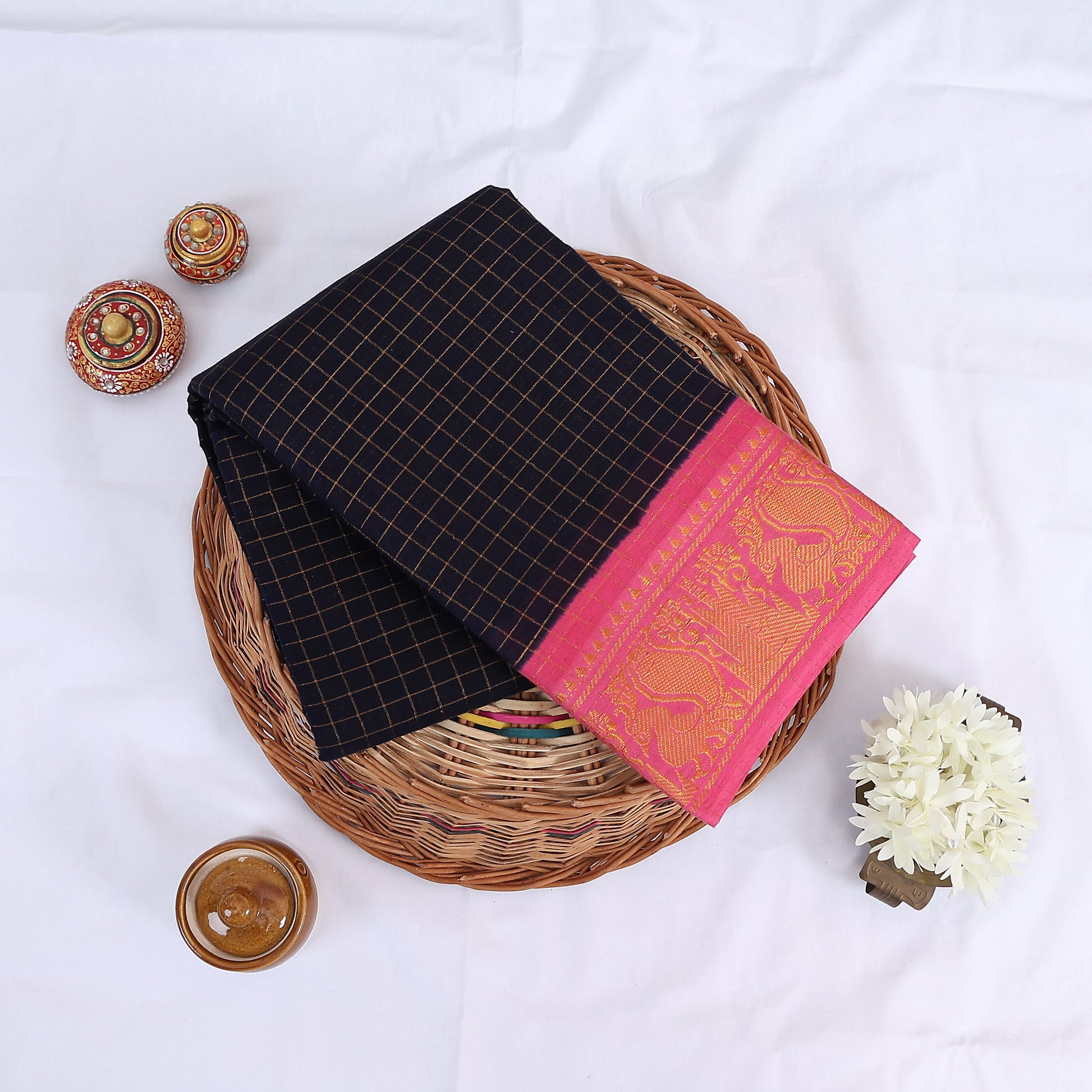 Sungudi cotton saree with gold zari checks body and navy blue peacock motif border folded top view on wicker basket