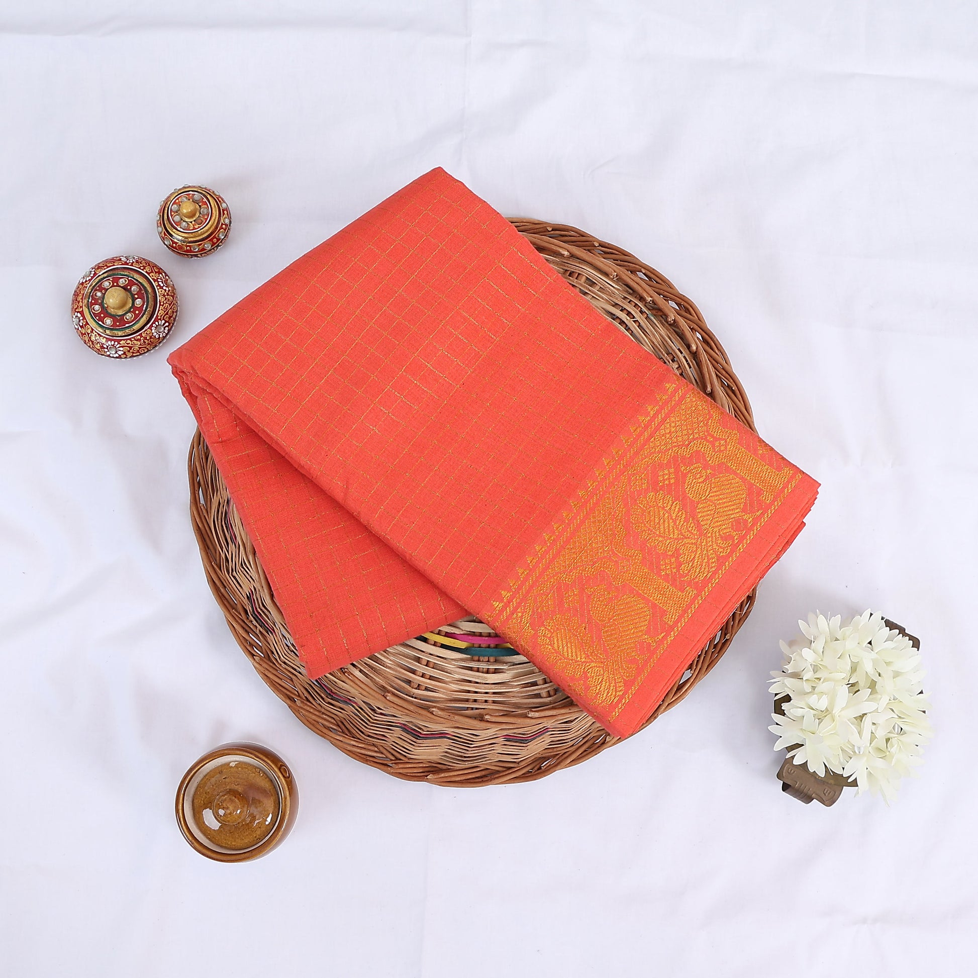 Sungudi cotton saree with gold zari checks body and orange peacock motif border folded top view on wicker basket