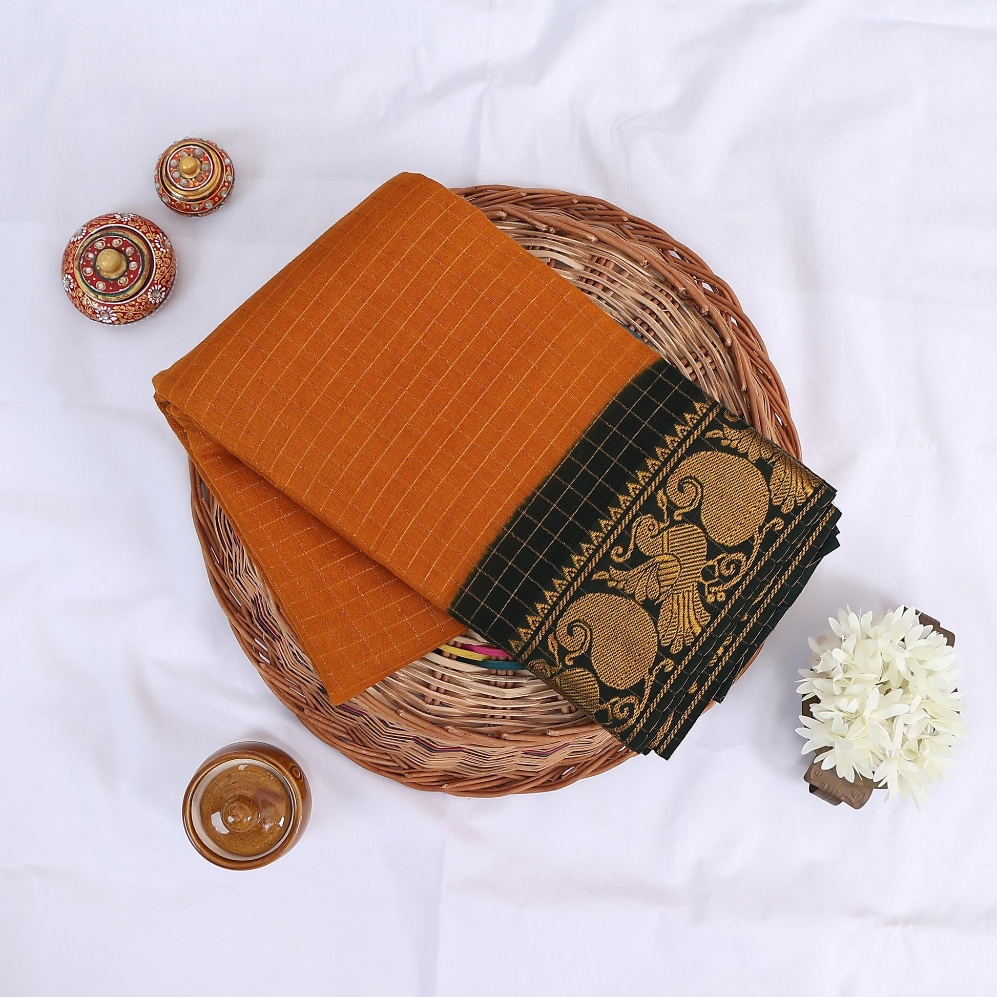 Sungudi cotton saree with gold zari checks body and green peacock motif border folded top view on wicker basket