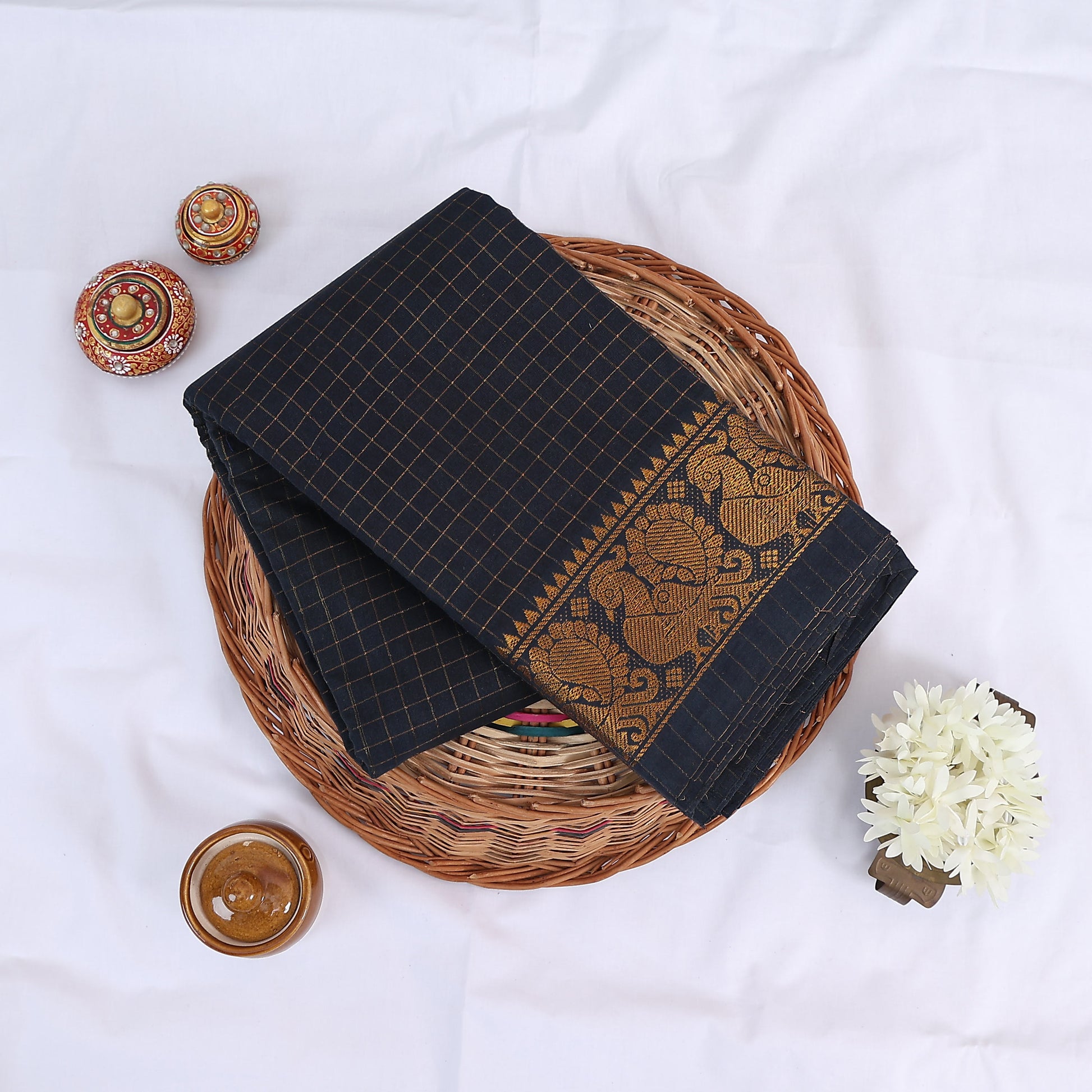 Sungudi cotton saree with gold zari checks body and navy blue peacock motif border folded top view on wicker basket