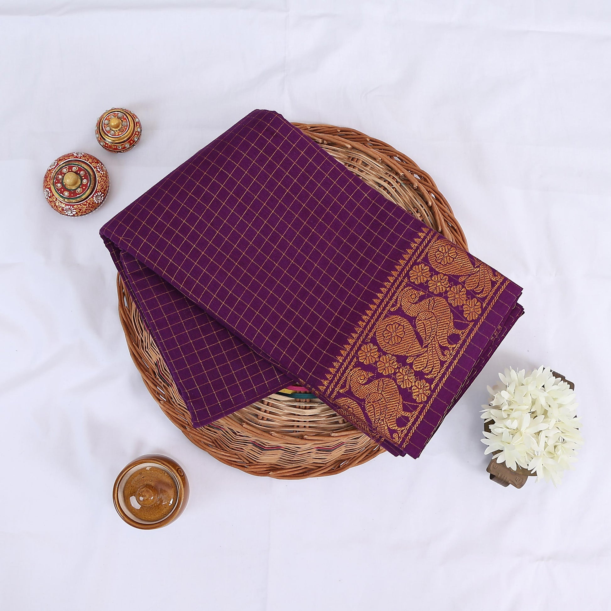 Sungudi cotton saree with gold zari checks body and purple peacock motif border folded top view on wicker basket