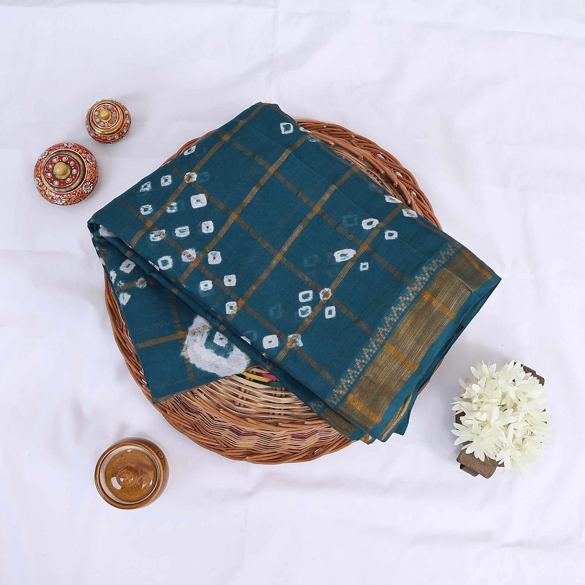 Sungudi cotton saree with white tie dye motifs and gold checkered pattern in teal blue folded top view with zari border