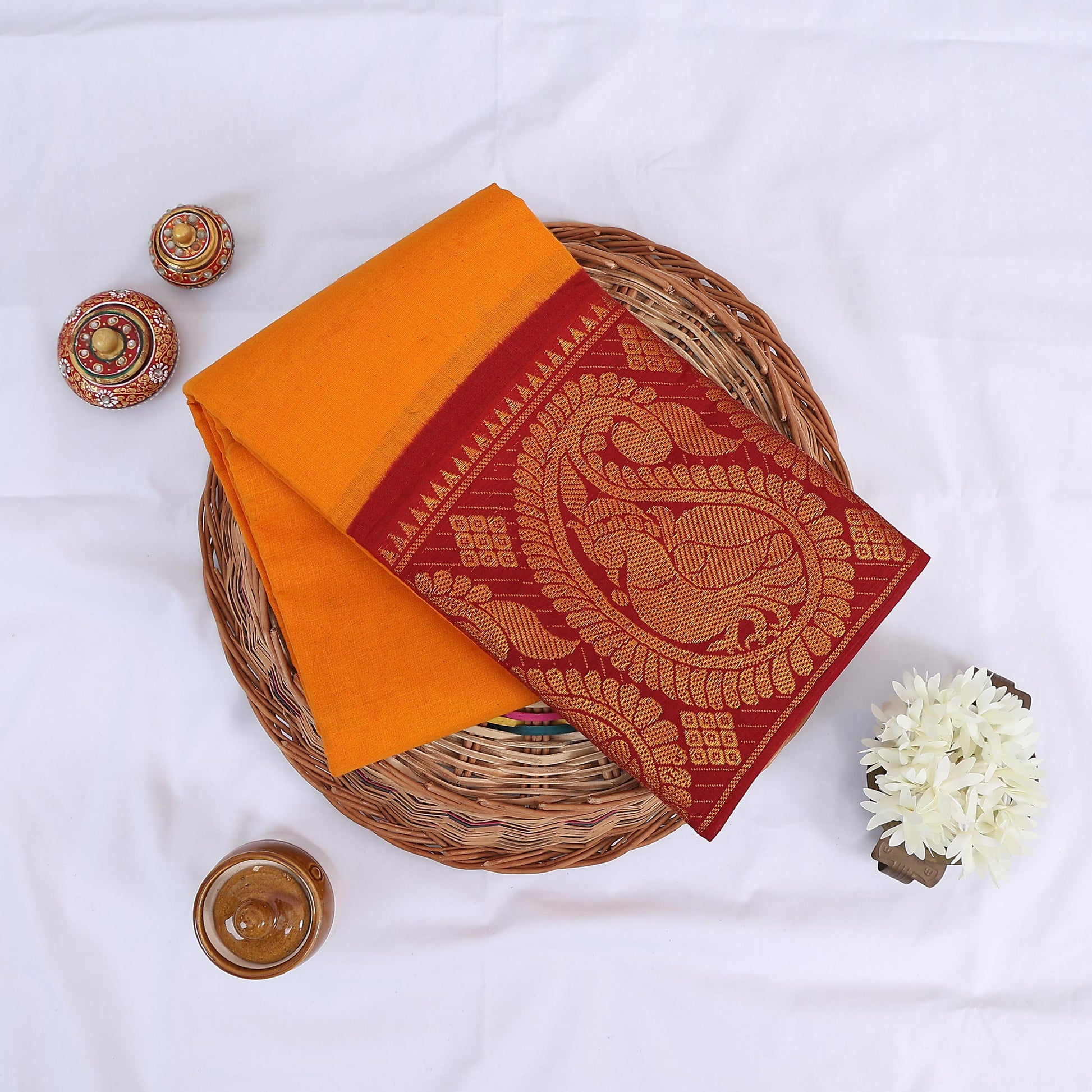 Sungudi cotton saree with yellow body and maroon gold zari pallu top view folded on wicker basket