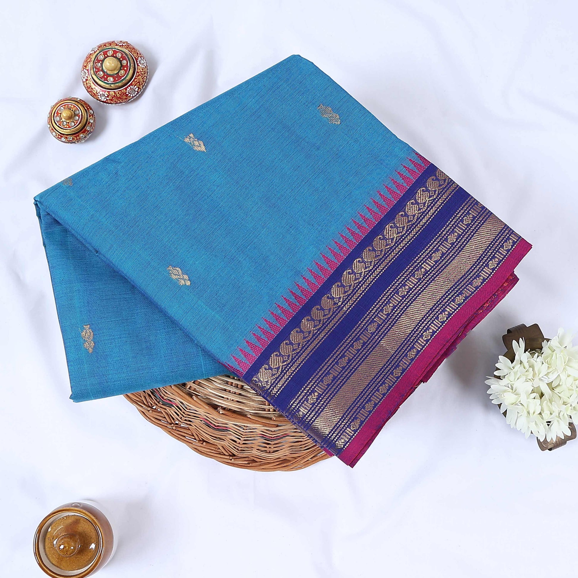 Sky blue Venkatagiri cotton saree with gold zari buttas and royal blue zari border folded flat lay view.