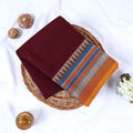 Maroon Venkatagiri cotton saree with blue and gold geometric zari woven border folded flat lay front view.