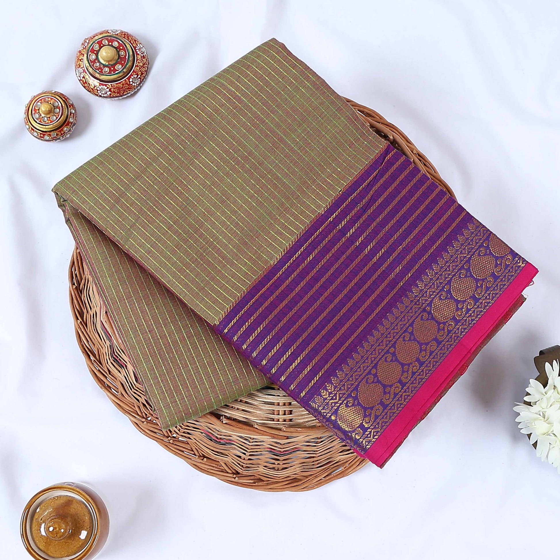 Venkatagiri cotton saree with gold stripes purple zari border and pink edge folded top view on wicker tray.