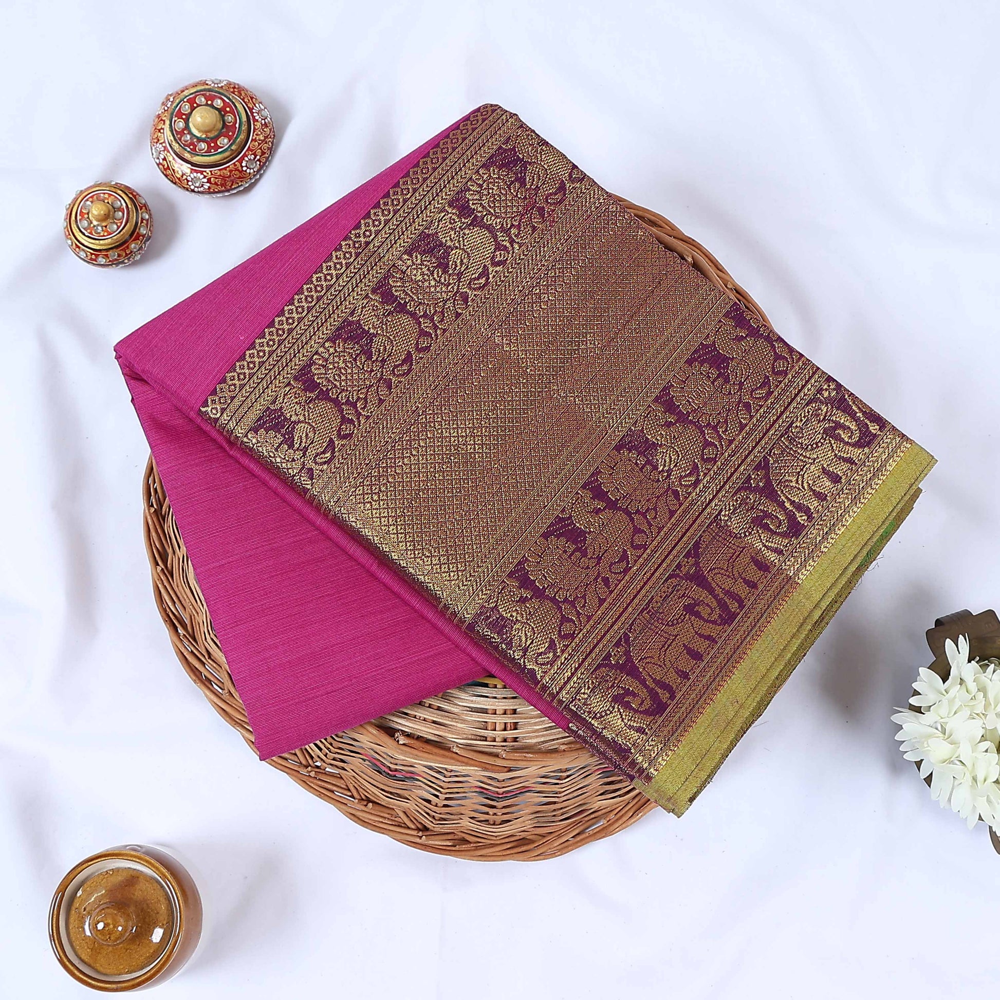 Venkatagiri cotton saree with gold zari floral and elephant border in pink folded top view on wicker basket.