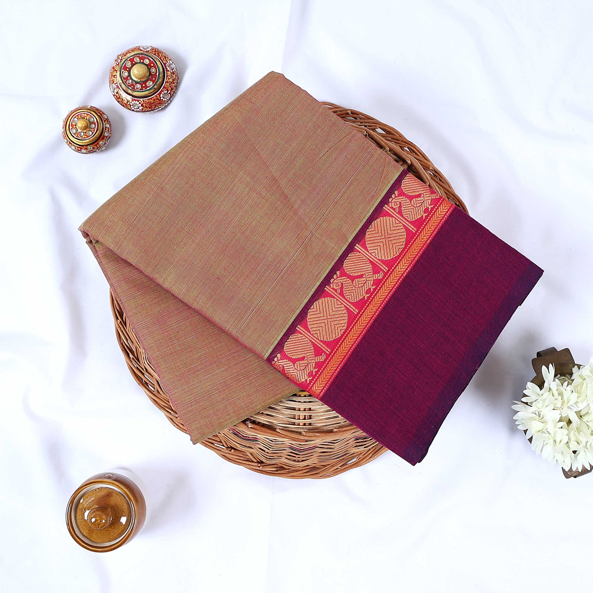 Venkatagiri cotton saree with olive body and maroon zari border folded top view on wicker basket