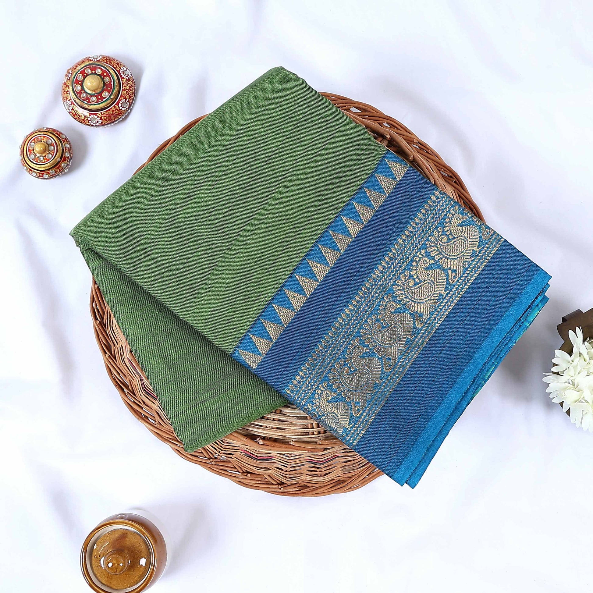 Venkatagiri cotton saree with green body blue peacock zari border folded front view on wicker basket