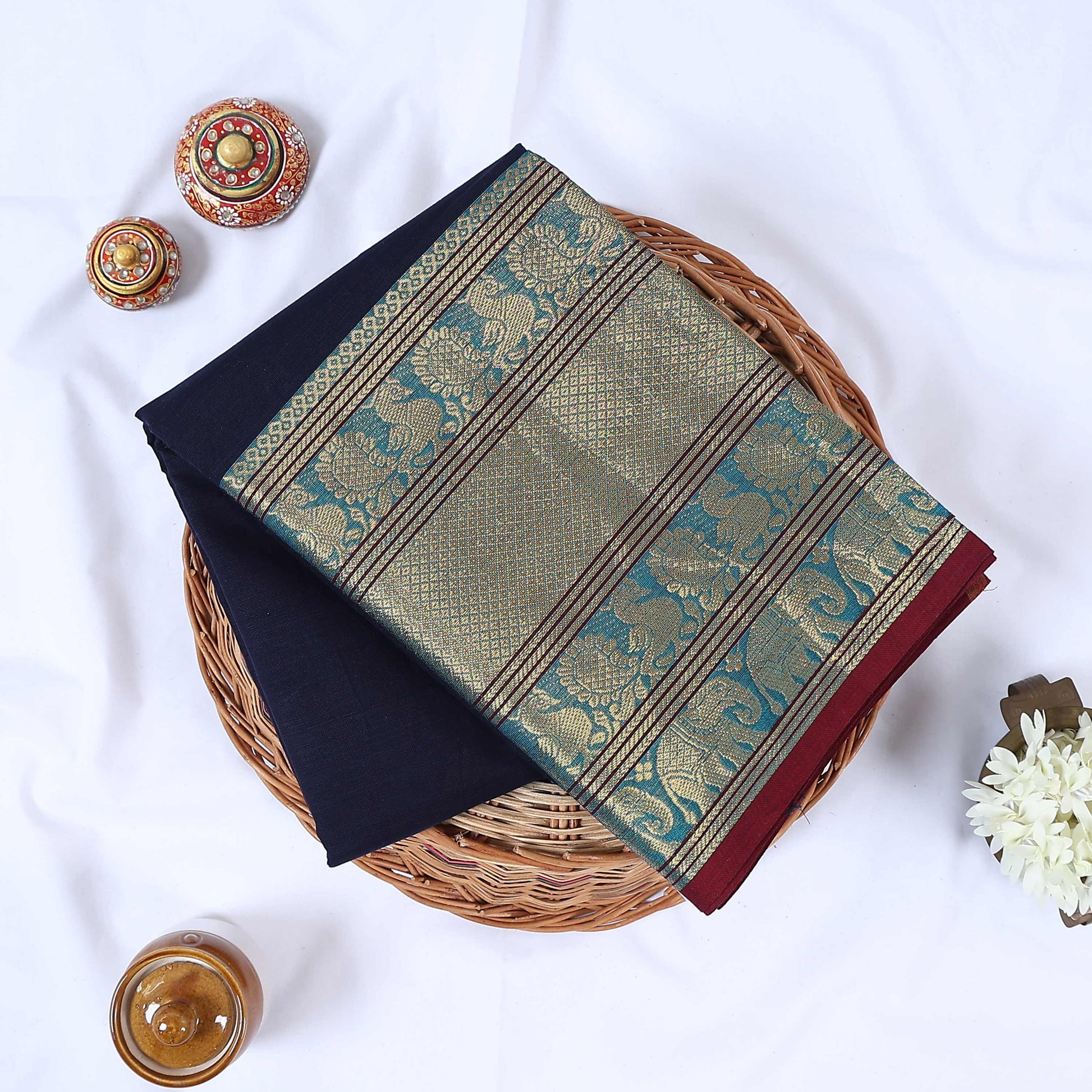 Venkatagiri cotton saree with gold zari floral and elephant border in navy blue folded top view on wicker basket.