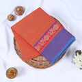 Venkatagiri cotton saree with orange body and purple zari border folded top view on wicker basket
