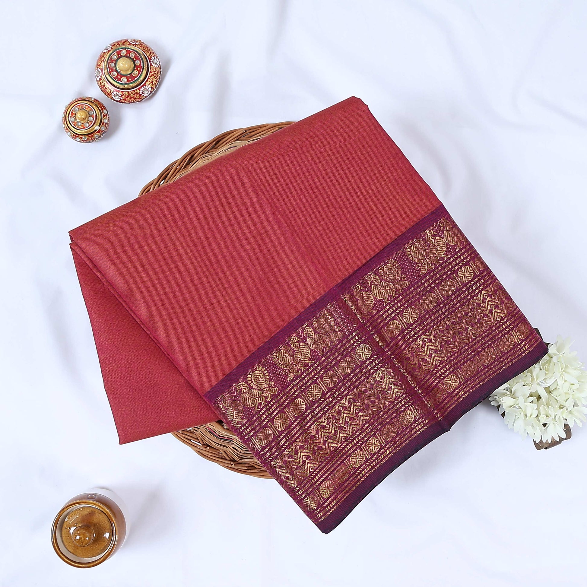 Venkatagiri cotton saree with pink body and maroon gold zari border folded flat lay top view.

