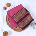 Venkatagiri cotton saree with purple zari border in pink folded flat on a wicker basket top view