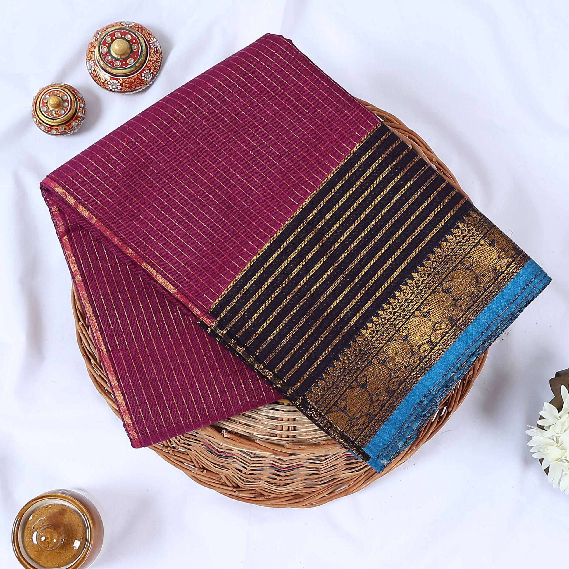 Venkatagiri cotton saree with gold stripes black zari border and blue edge folded top view on wicker tray.