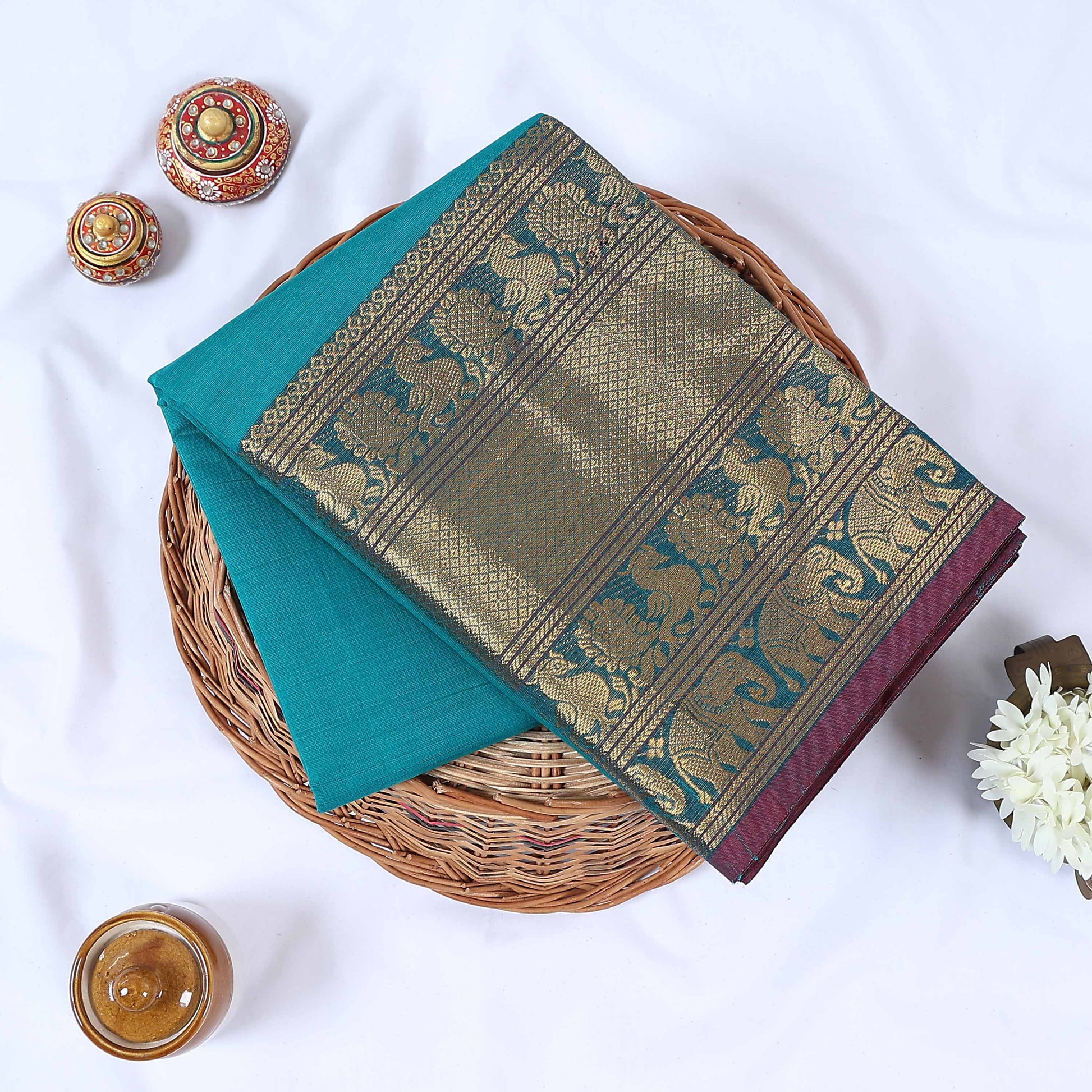 Venkatagiri cotton saree with gold zari floral and elephant border in blue  folded top view on wicker basket.