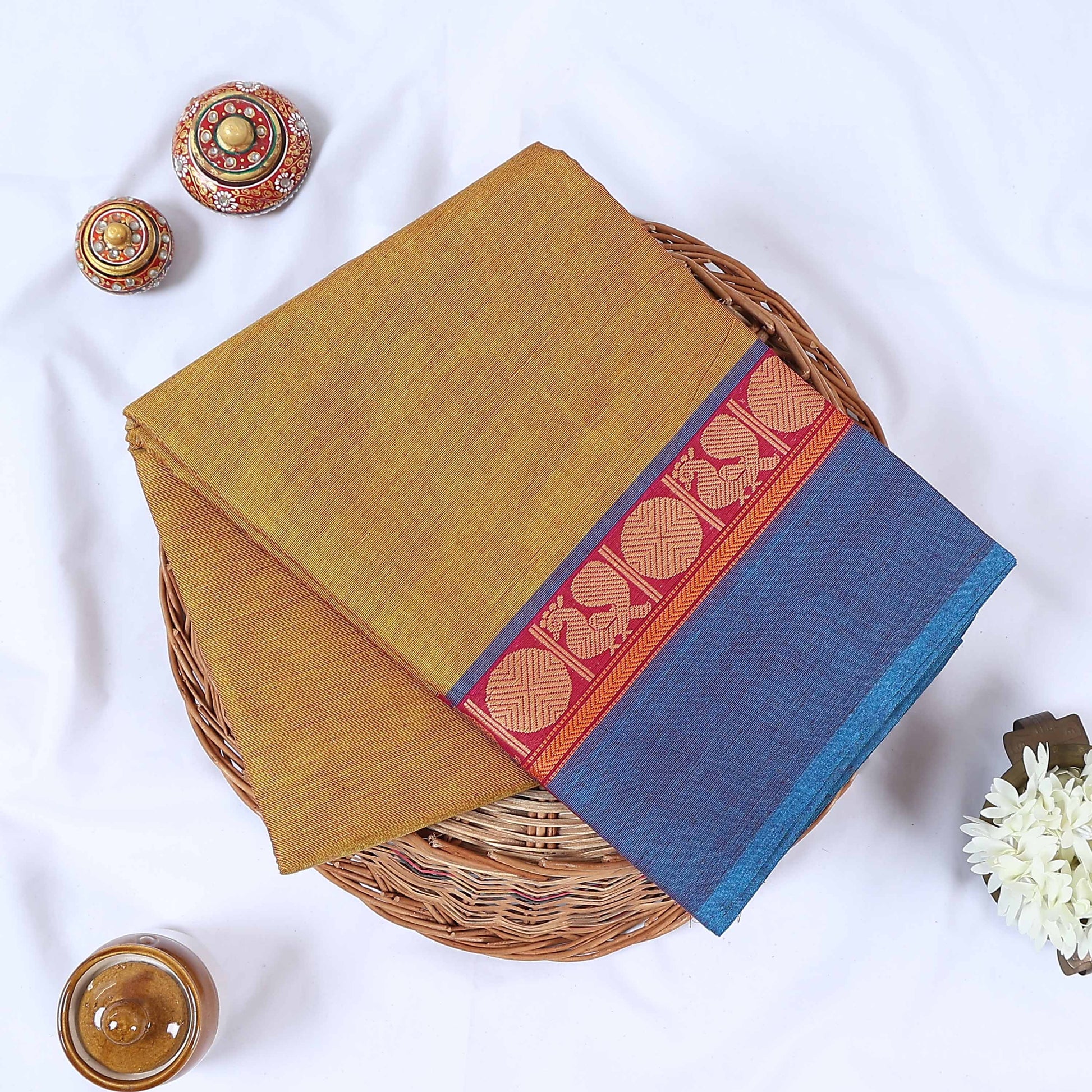 Venkatagiri cotton saree with yellow body and blue zari border folded top view on wicker basket