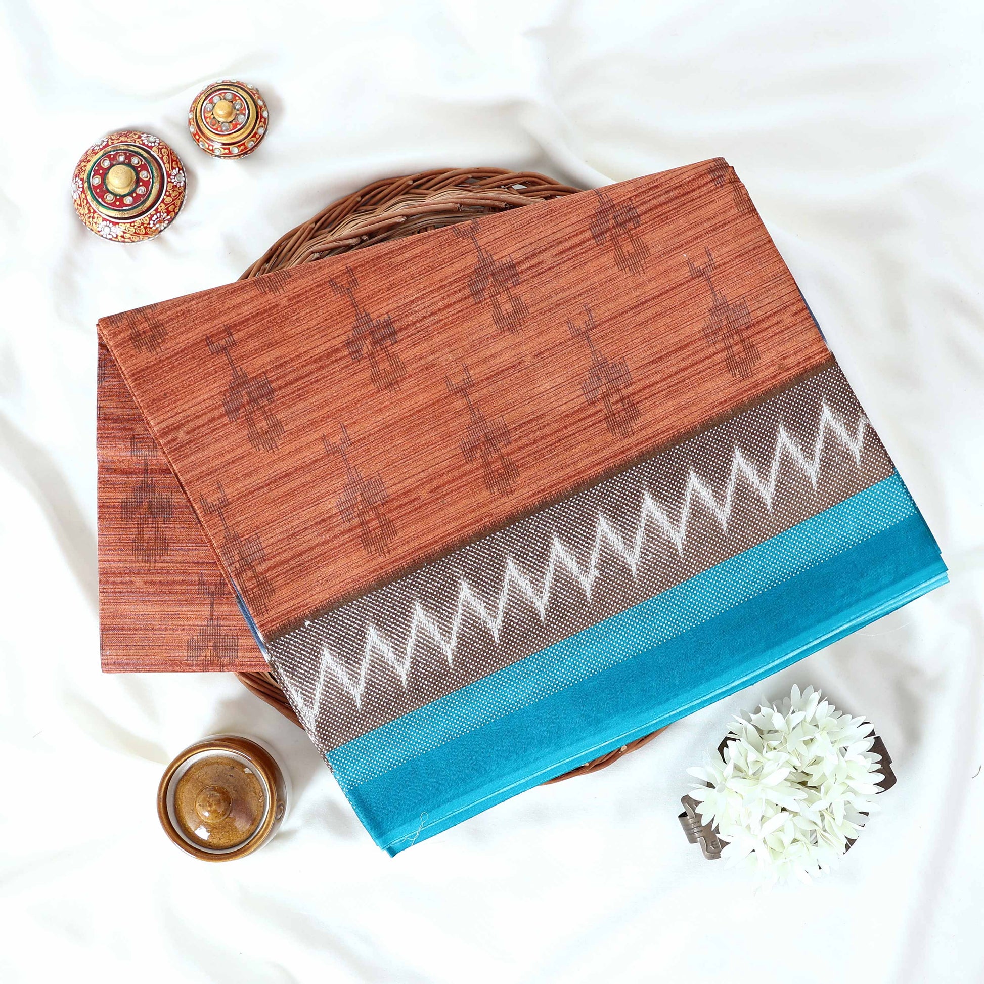 Brown voile cotton saree with ikat printed pattern and contrast chevron zari border, folded top view display