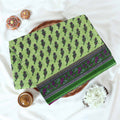 Voile cotton saree with floral motif print and decorative border in green folded flat lay view on woven basket.