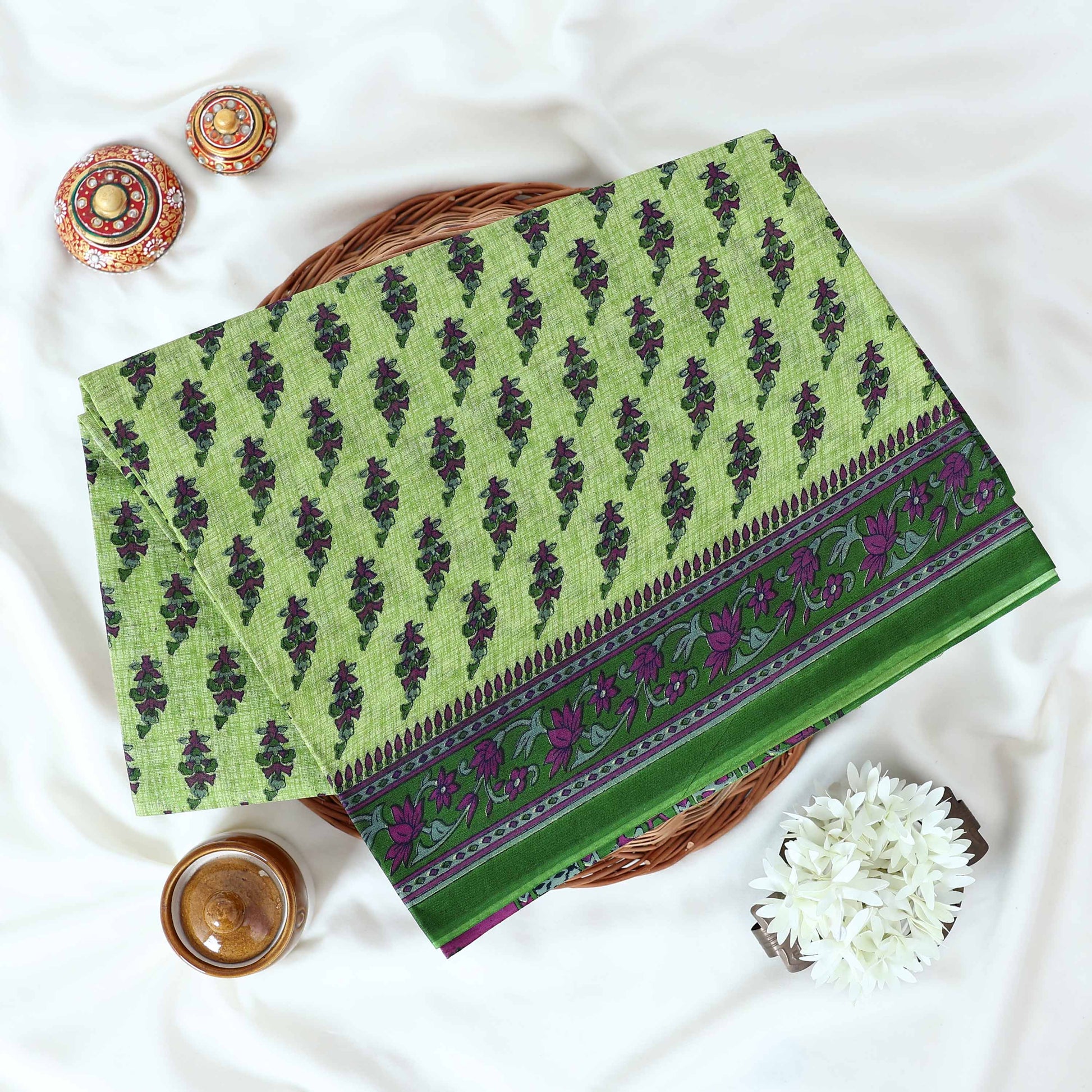 Voile cotton saree with floral motif print and decorative border in green folded flat lay view on woven basket.