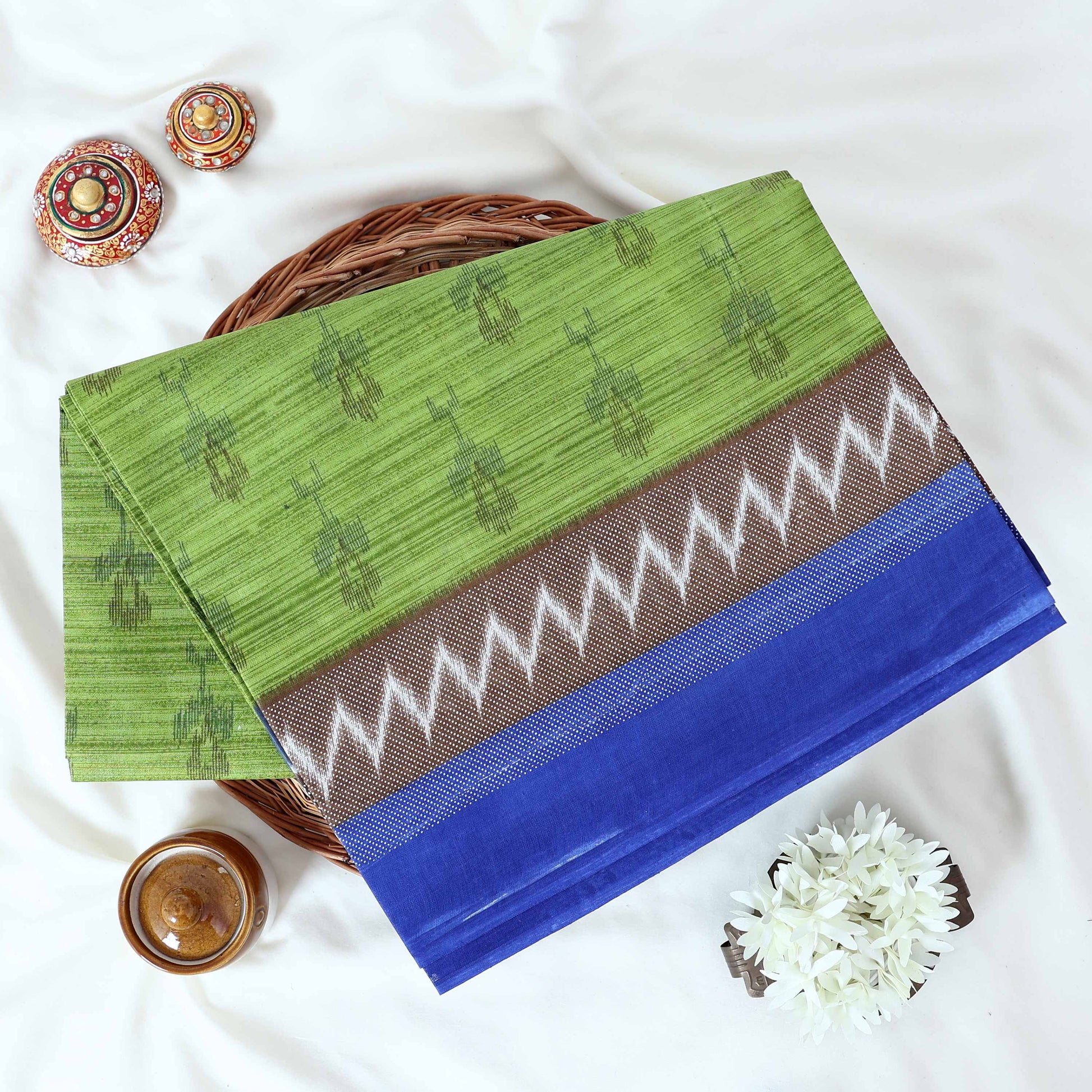 Green voile cotton saree with ikat printed pattern and contrast chevron zari border folded top view display