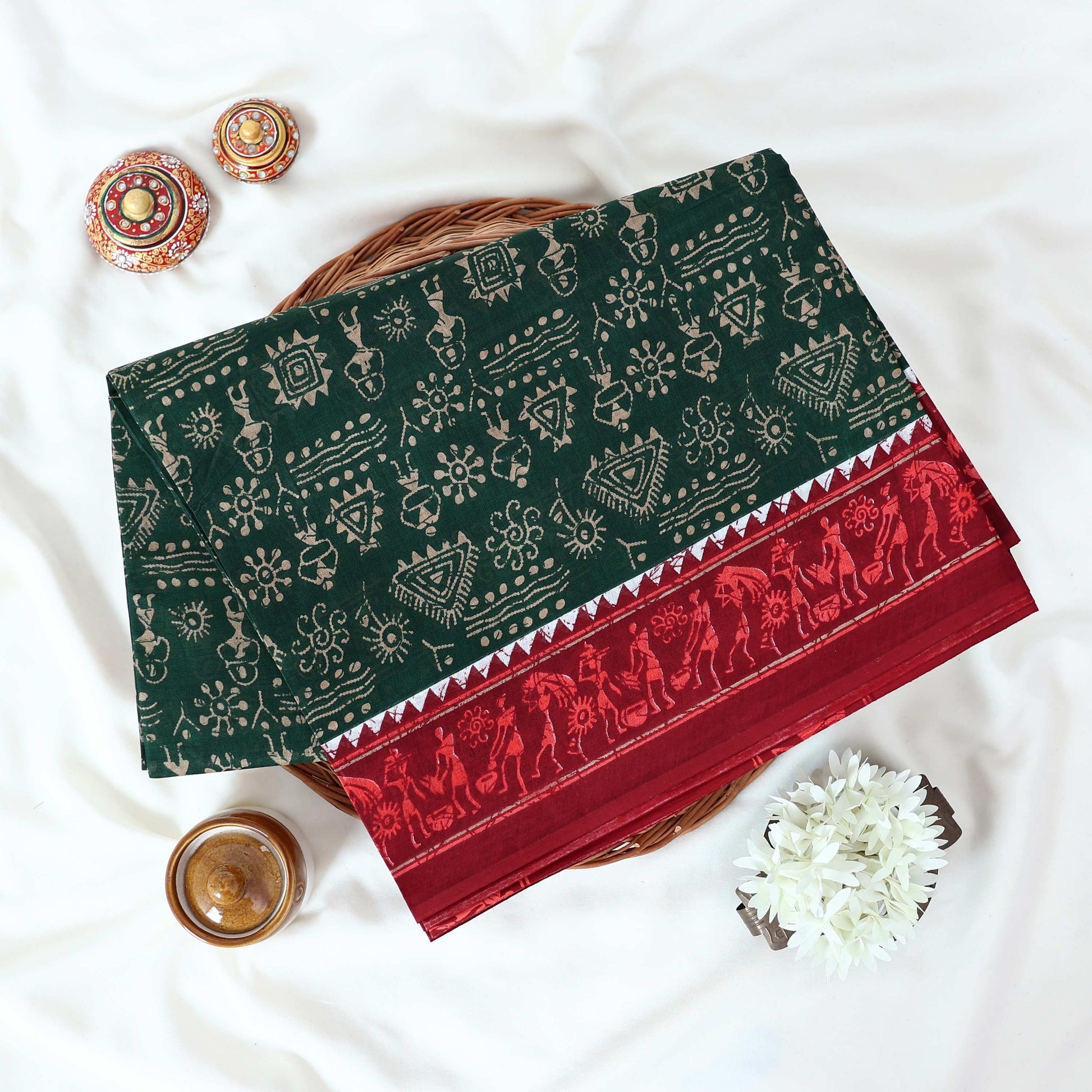 Green Voile cotton saree with tribal print body and red contrast folk art border folded top view 