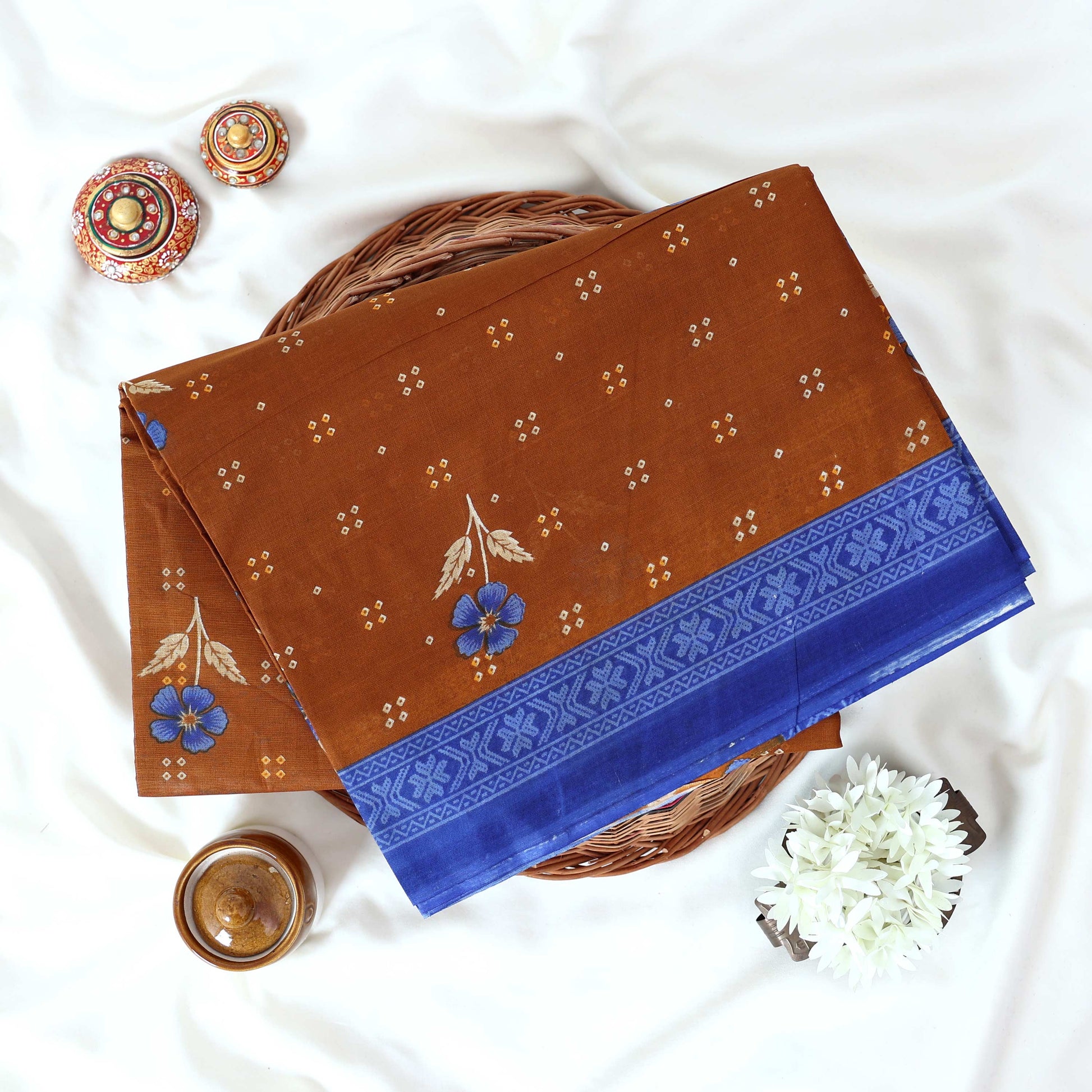 Brown Voile cotton saree with floral motifs butta body pattern and blue floral motif border folded top view