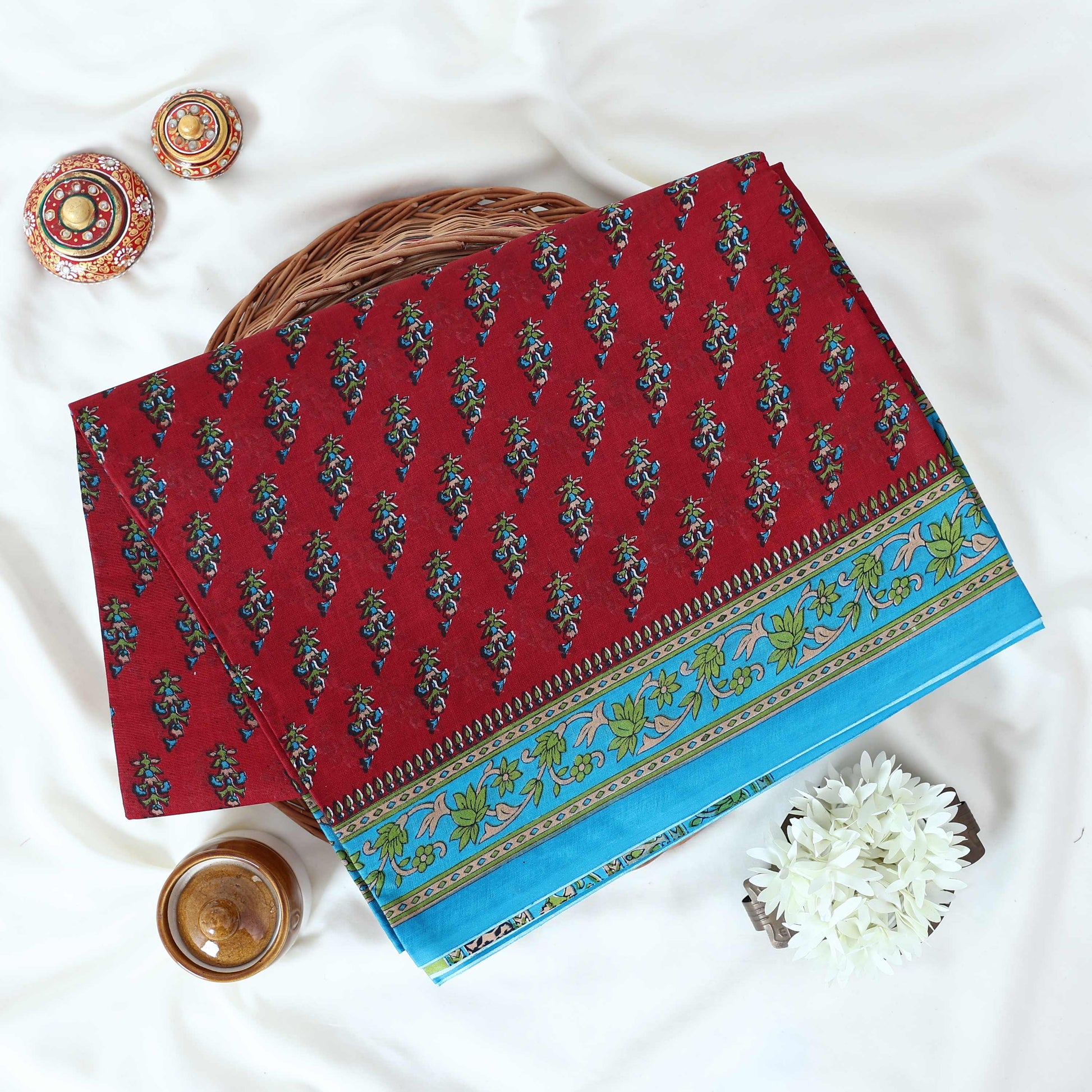 Voile cotton saree with floral motif print and decorative border in maroon folded flat lay view on woven basket.