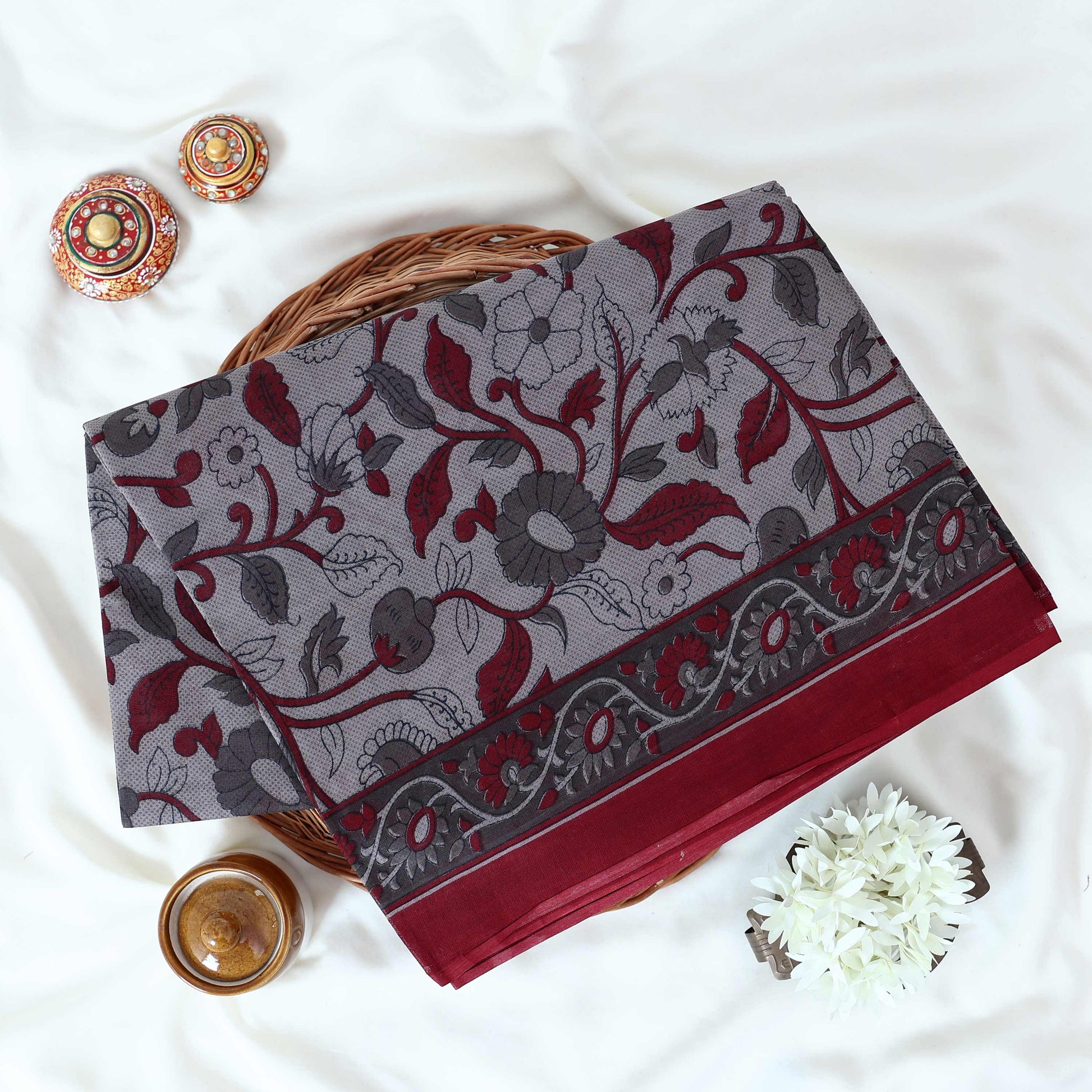 Maroon Voile cotton saree with floral vine print and contrast border, neatly folded in a top view product display.