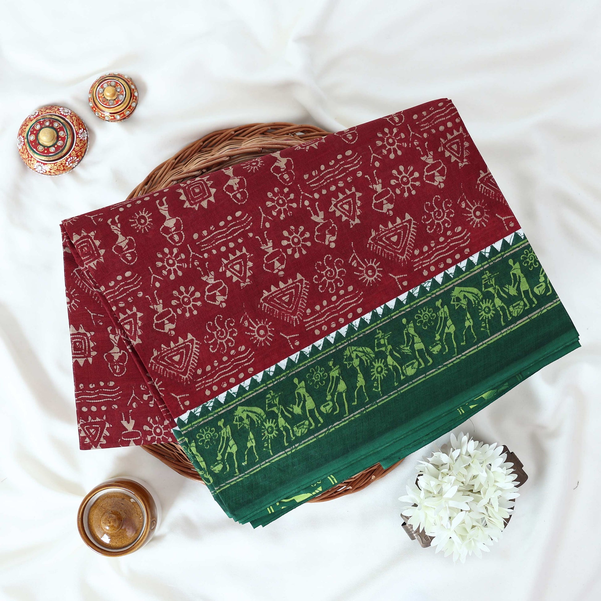 Maroon Voile cotton saree with tribal print body and green contrast folk art border folded top view 