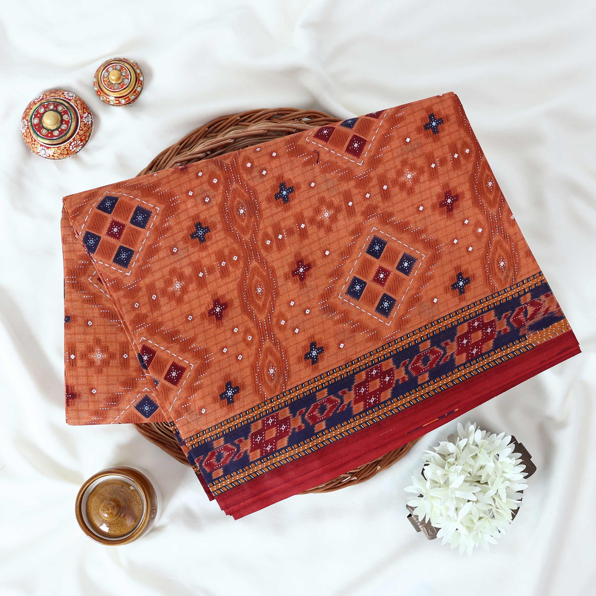 Voile cotton saree with geometric ethnic print and contrast border in rust orange top view folded display