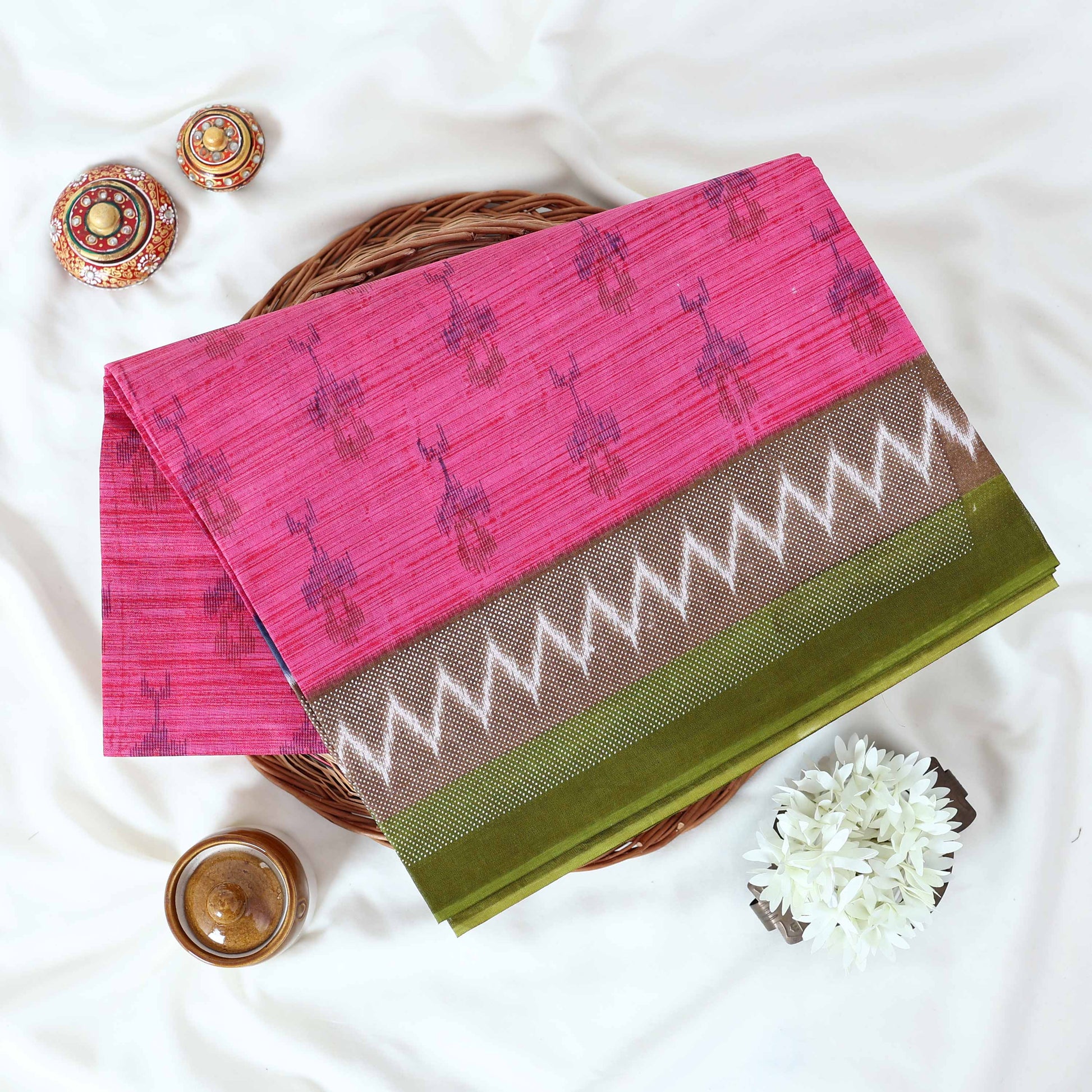 Pink voile cotton saree with ikat printed pattern and contrast chevron zari border folded top view display