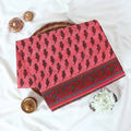 Voile cotton saree with floral motif print and decorative border in pink folded flat lay view on woven basket.