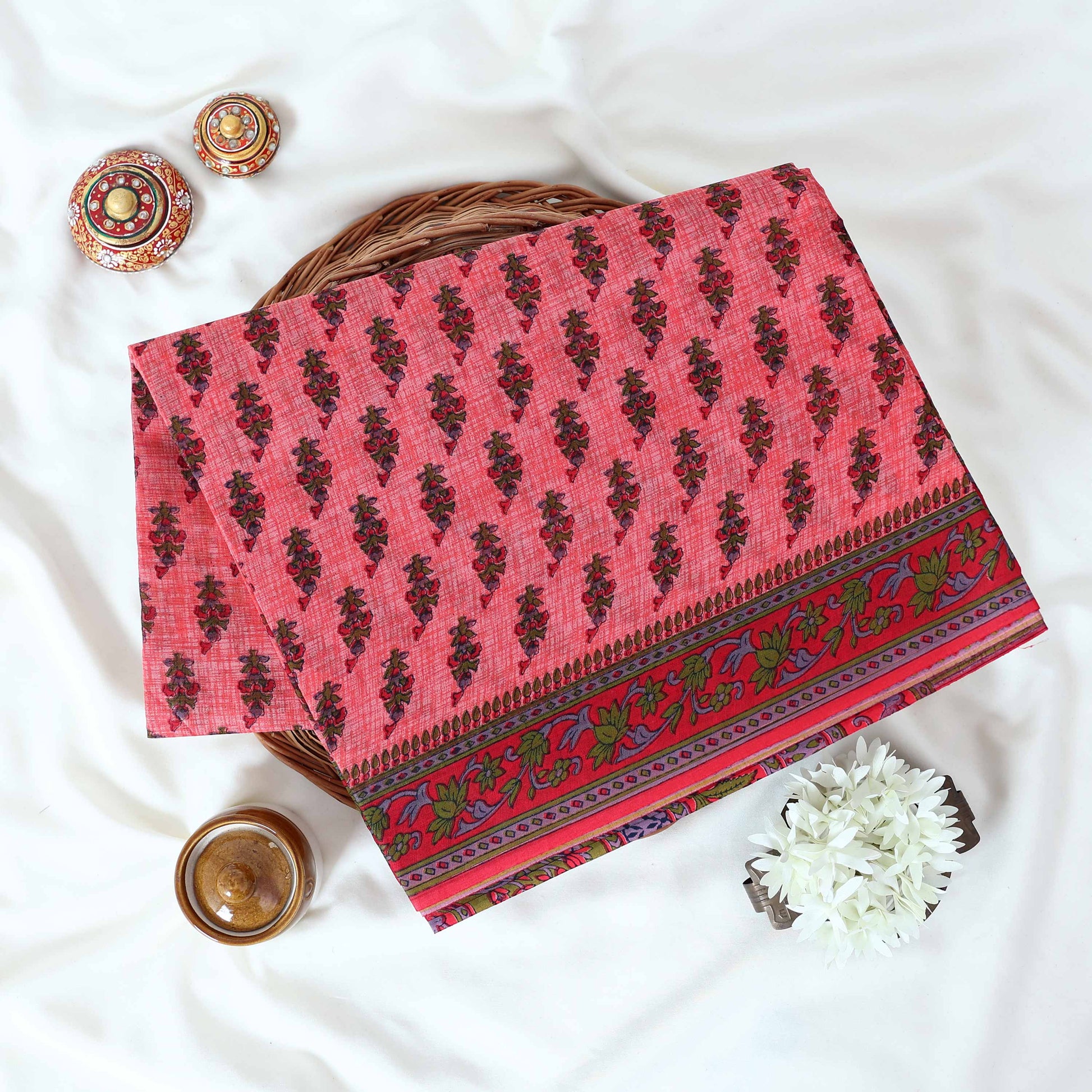 Voile cotton saree with floral motif print and decorative border in pink folded flat lay view on woven basket.