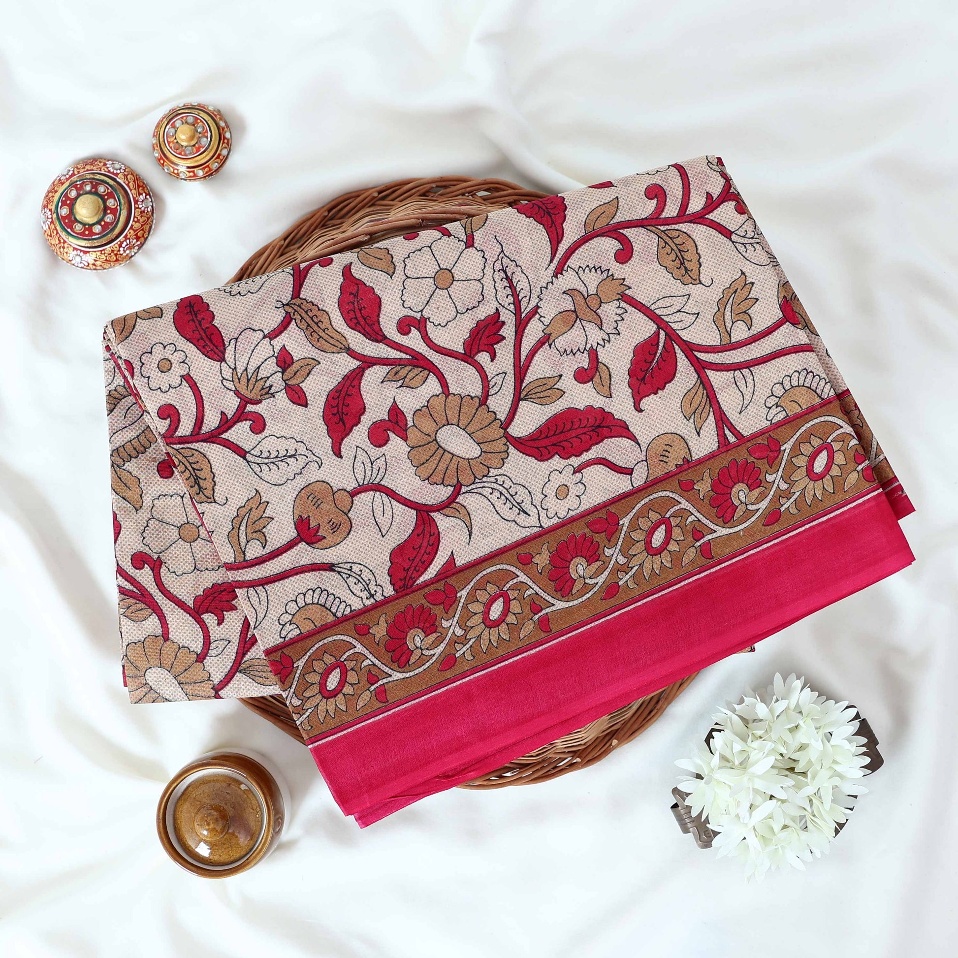 Pink Voile cotton saree with floral vine print and contrast border neatly folded in a top view product display.