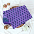 Voile cotton saree with floral motif print and decorative border in purple folded flat lay view on woven basket.
