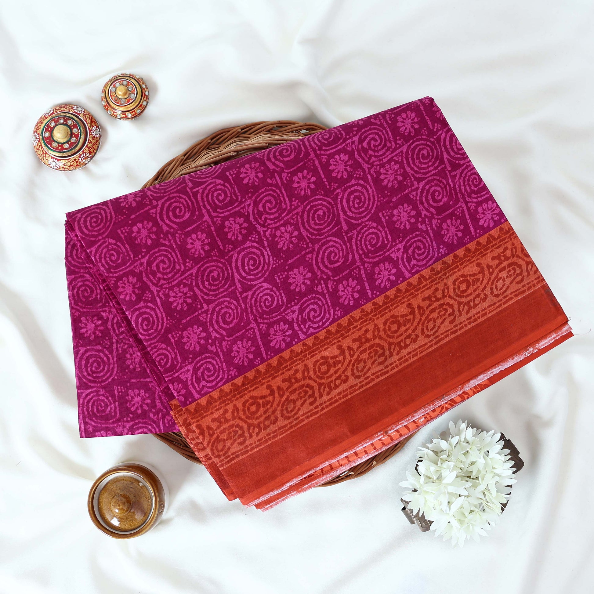Purple Voile cotton saree with spiral and floral printed motifs contrast border front flat lay view on a woven basket.