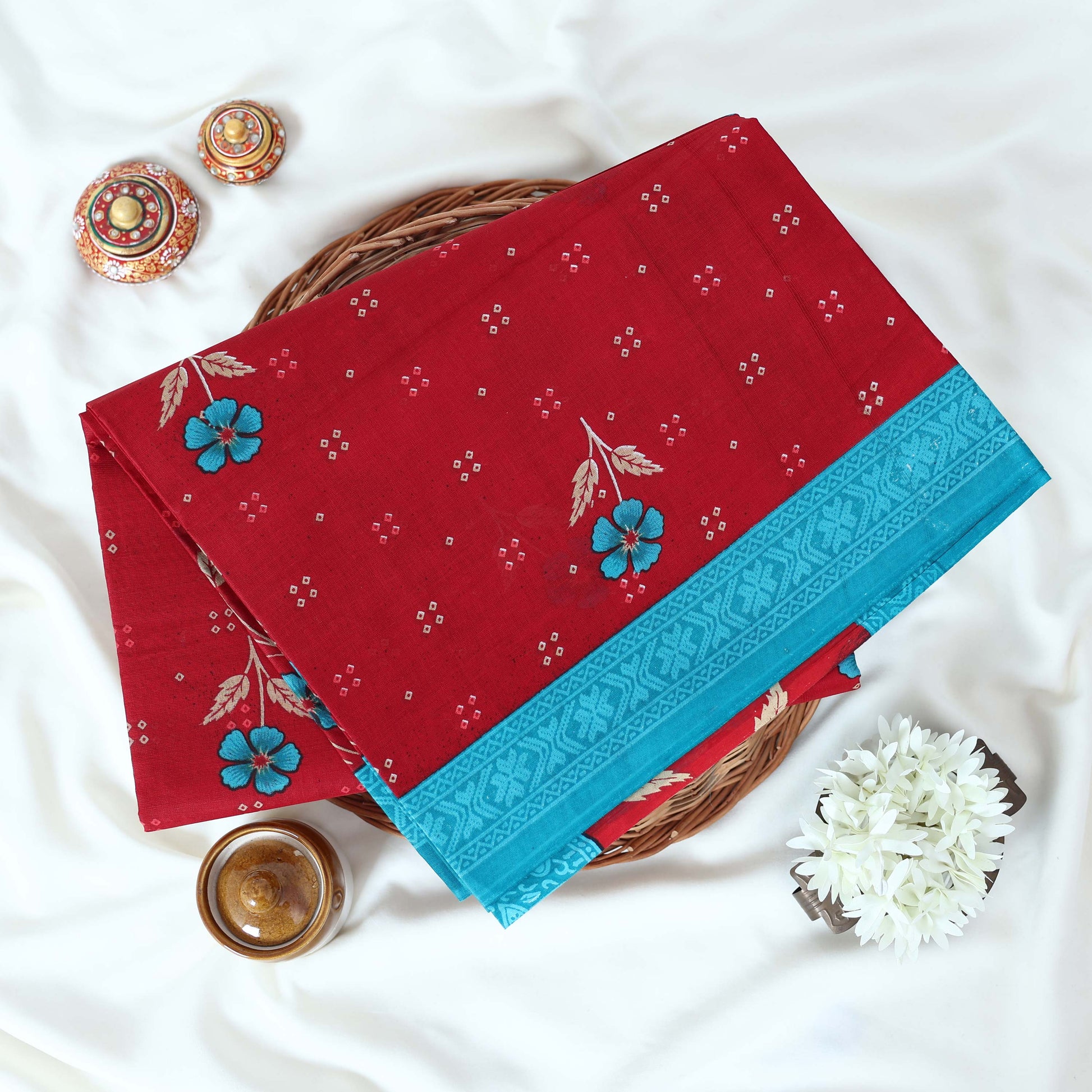 Red Voile cotton saree with floral motifs butta body pattern and blue floral motif border folded top view
