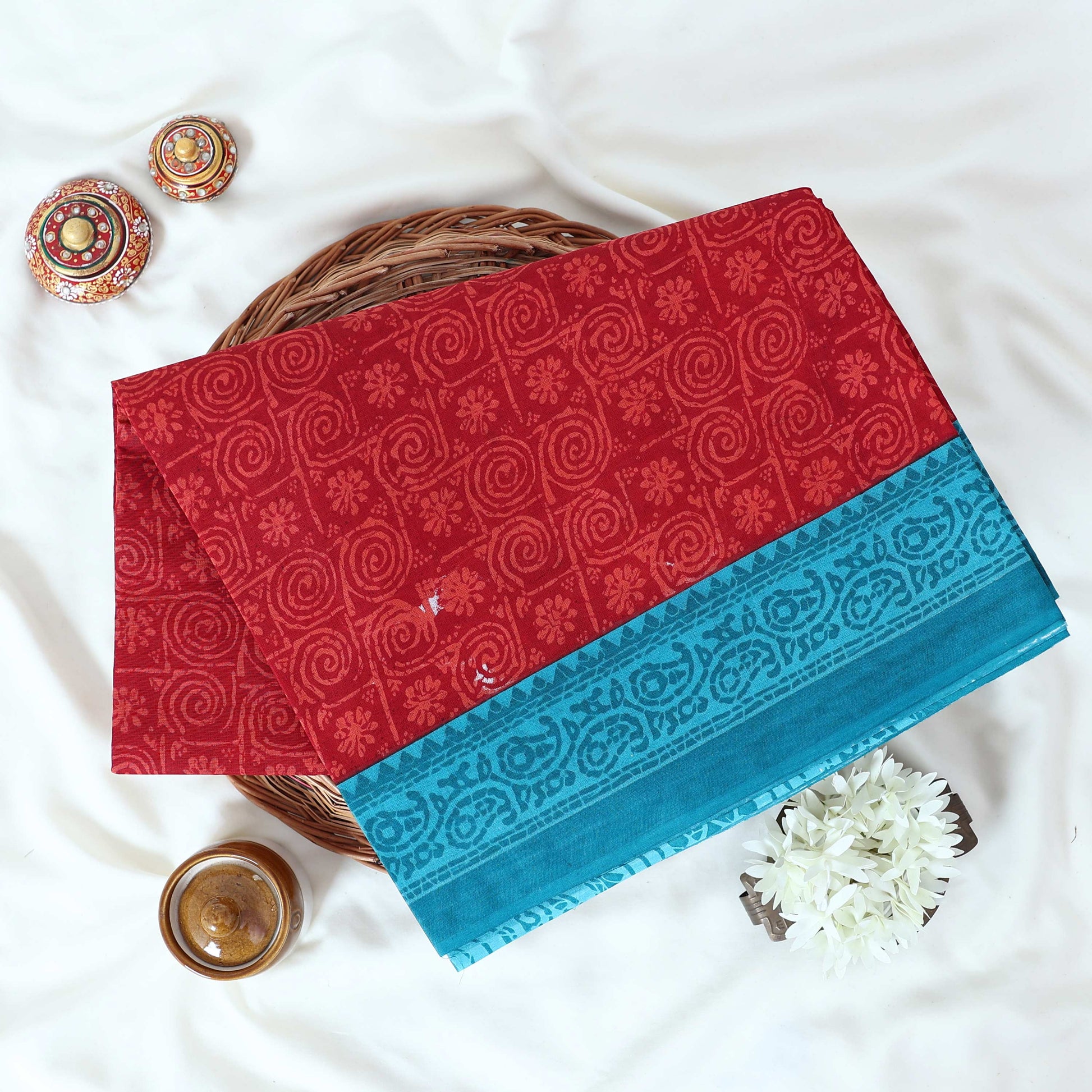 Red Voile cotton saree with spiral and floral printed motifs contrast border front flat lay view on a woven basket.