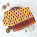 Mustard yellow voile cotton saree with floral border and traditional red motifs folded flat lay product display.