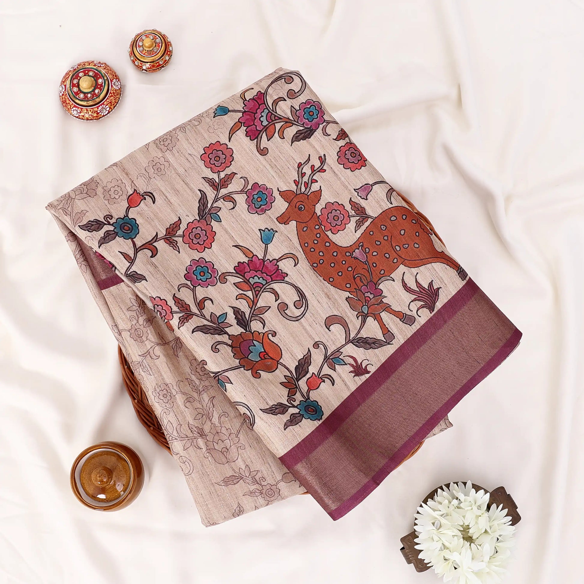 A folded beige cotton saree with a brown deer and floral vine print, displayed 
