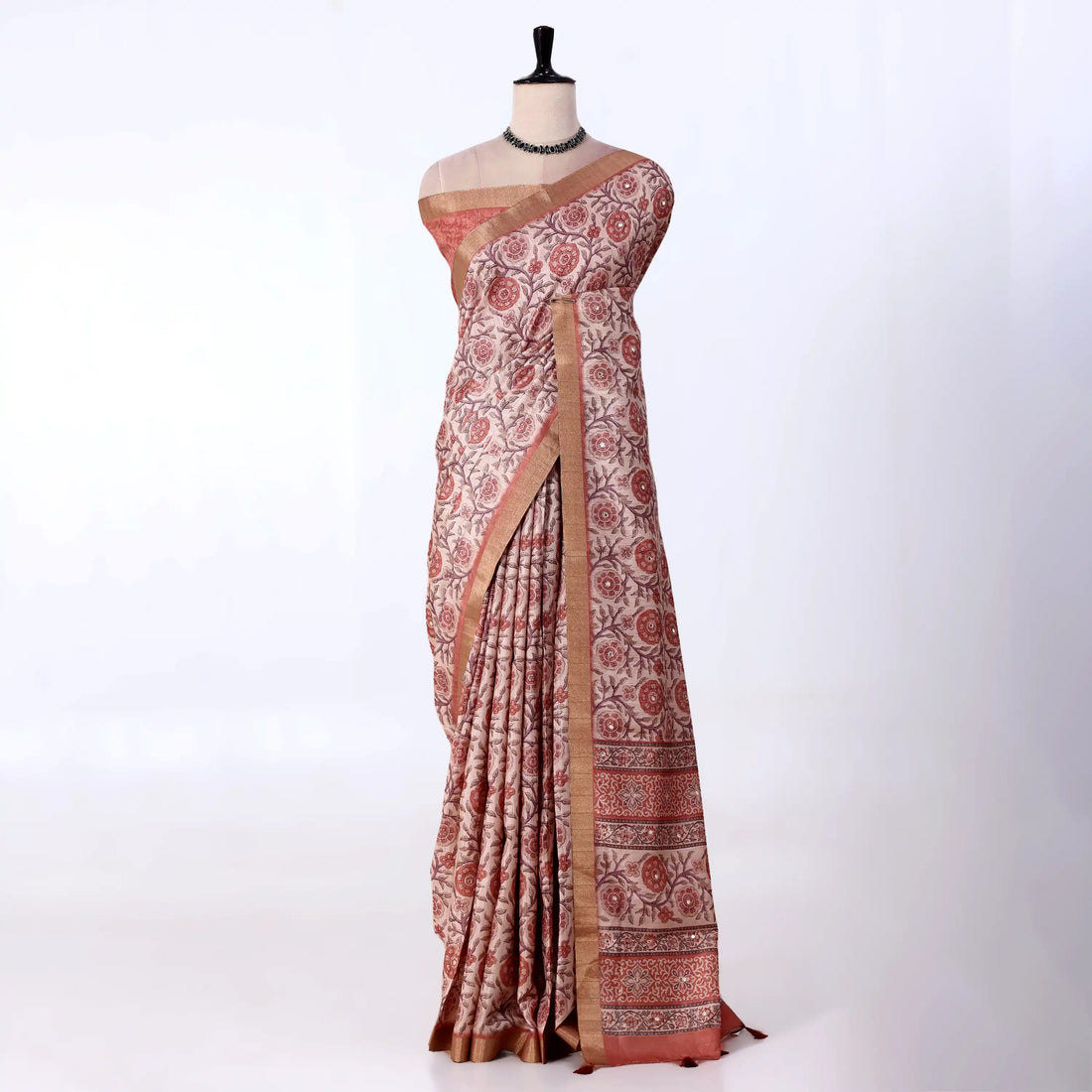 A traditional Indian saree features a rust-red and beige floral block print pattern with a solid rust-red border and a metallic gold zari.