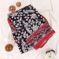 A folded black and red printed saree features a red base with black and white floral patterns and a solid red border.