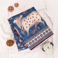 A folded textile product with a hand-painted style cow motif in blue, cream, and red.