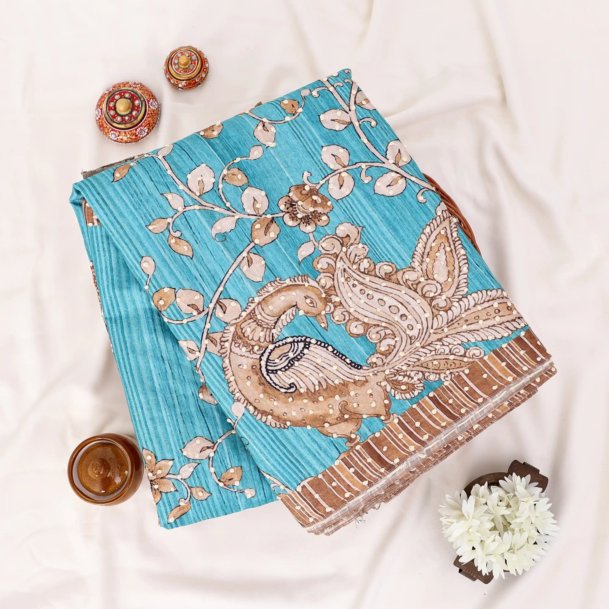 A folded blue saree with a beige and brown paisley and floral print