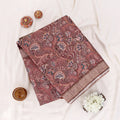 A folded deep brown saree with intricate gold and beige floral patterns